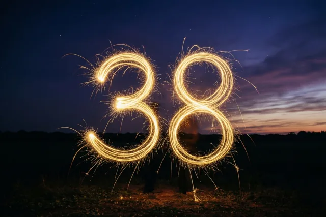Gouden lichtsporen van sterretjes vormen 38 boven een veld bij schemering, tegen een donkere hemel met een zwakke zonsondergang aan de horizon.