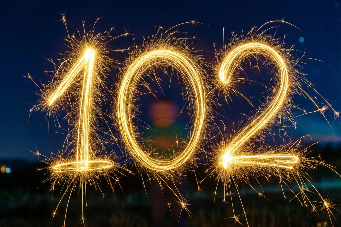 Gouden lichtsporen van sterretjes vormen het getal 102 tegen een diepblauwe nachthemel.