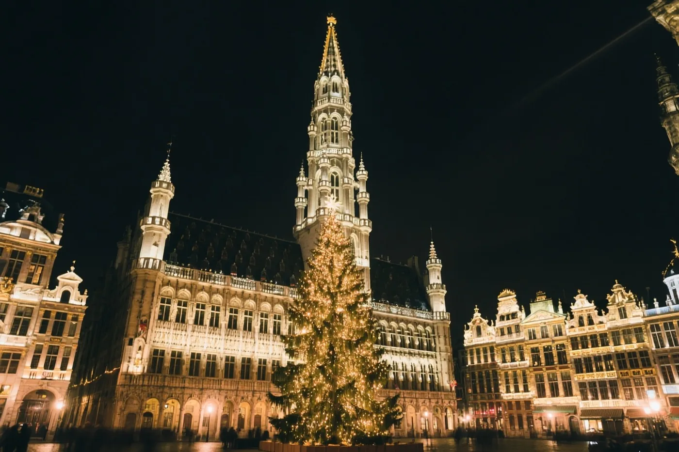 Op de Grote Markt in Brussel staat een hoge kerstboom met lichtjes tussen verlichte historische gildehuizen, in gouden en witte tinten tegen een donkere hemel.