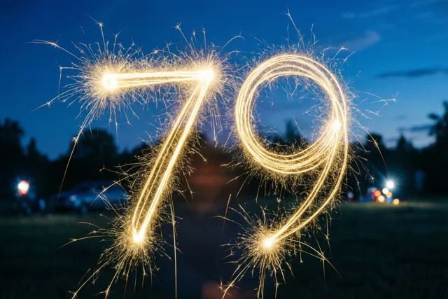 Gouden lichtsporen van sterretjes vormen het getal 79 tegen een donkerblauwe nachthemel, met onscherpe lichtjes op de achtergrond.