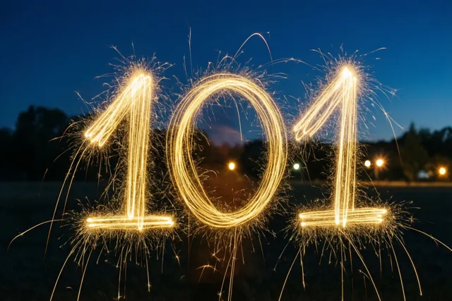 Gouden lichtsporen van sterretjes vormen 101 in de nacht, met lichtjes in de verte.