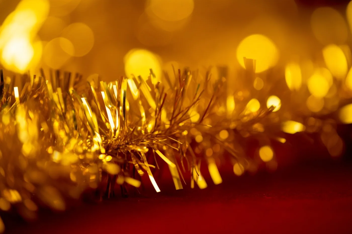 Een gouden glitterslinger vangt het licht voor een onscherpe achtergrond met gouden lichtvlekken en een dieprood oppervlak.