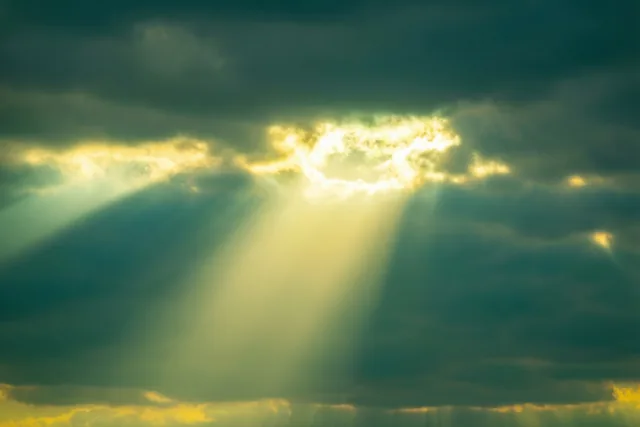 Fel goudkleurig zonlicht breekt door zware donkere wolken in een lucht met diepblauwe, grijze en groengekleurde tinten.