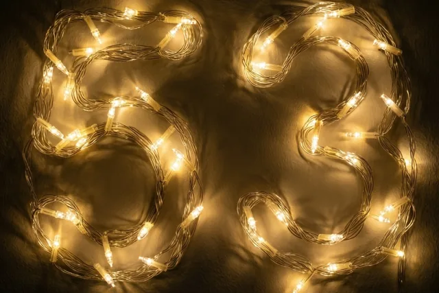 Goudgele lichtjes vormen het getal 53 op een donkere muur tegen een zwarte achtergrond.