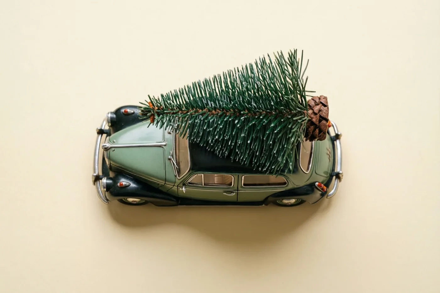 Een groen blikken speelgoedautootje in vintagestijl met een klein dennenboompje op het dak is van bovenaf te zien tegen een effen beige achtergrond.