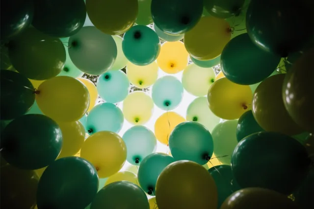 Pastelgroene en gele ballonnen vullen het beeld, van onderaf gezien naar een heldere lichtbron toe.