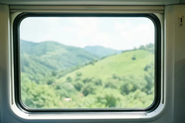 Vanuit een treinraam zijn zacht onscherpe groene heuvels onder een heldere hemel te zien, omlijst door het raam en het treininterieur.