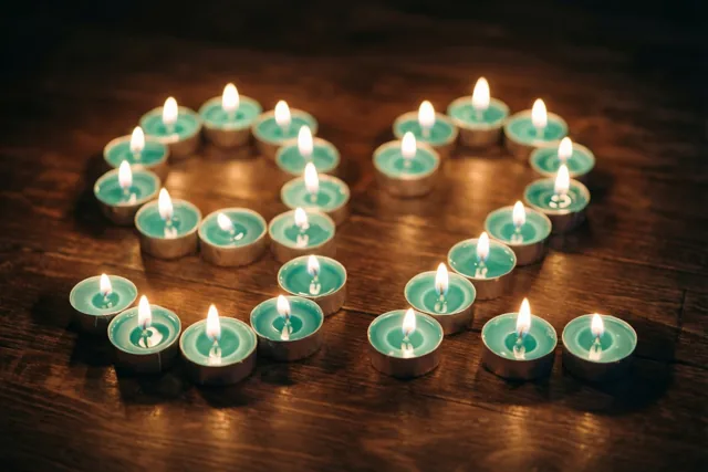 Brandende theelichtjes vormen een hart op een donkere houten vloer, met blauwgroene tinten en een warme gloed.
