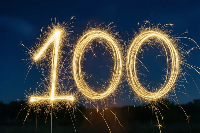 Gouden lichtsporen van sterretjes vormen het getal 100 tegen een donkere nachthemel.