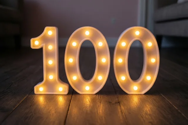 Warme lichtjes vormen het getal 100 op een donkere houten vloer.