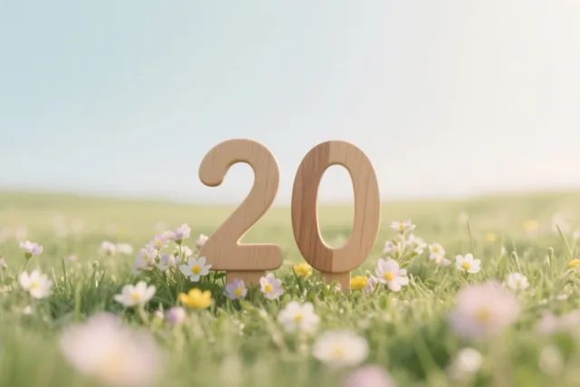 Houten cijfers vormen 20 in een veld met verse lentebloemen onder een heldere hemel, in warm zonlicht met een onscherpe achtergrond.