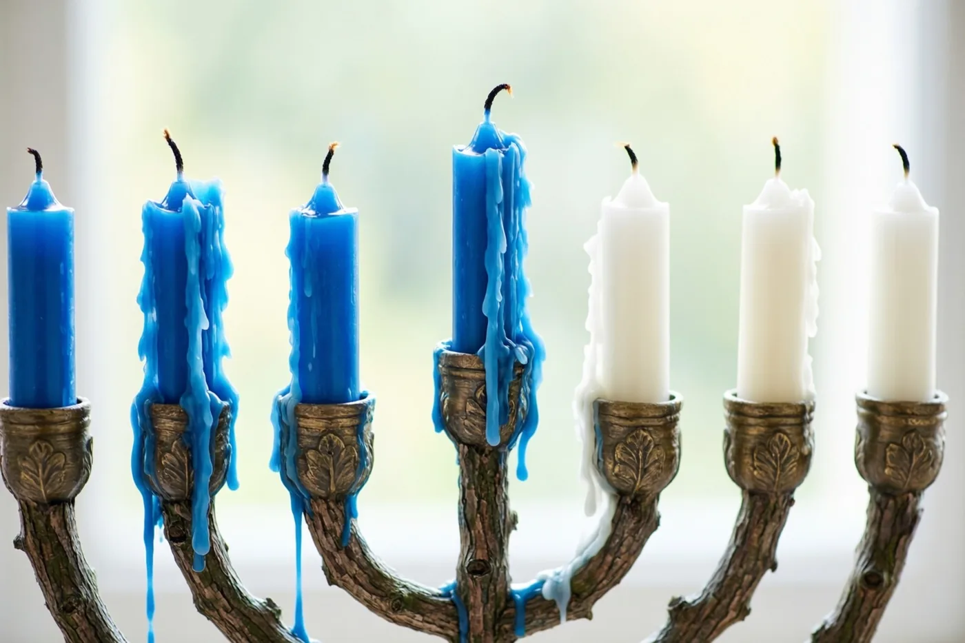 Een kandelaar met blauwe en witte kaarsen is van dichtbij te zien, met gesmolten was die langs enkele kaarsen en de armen druipt tegen een onscherpe achtergrond.