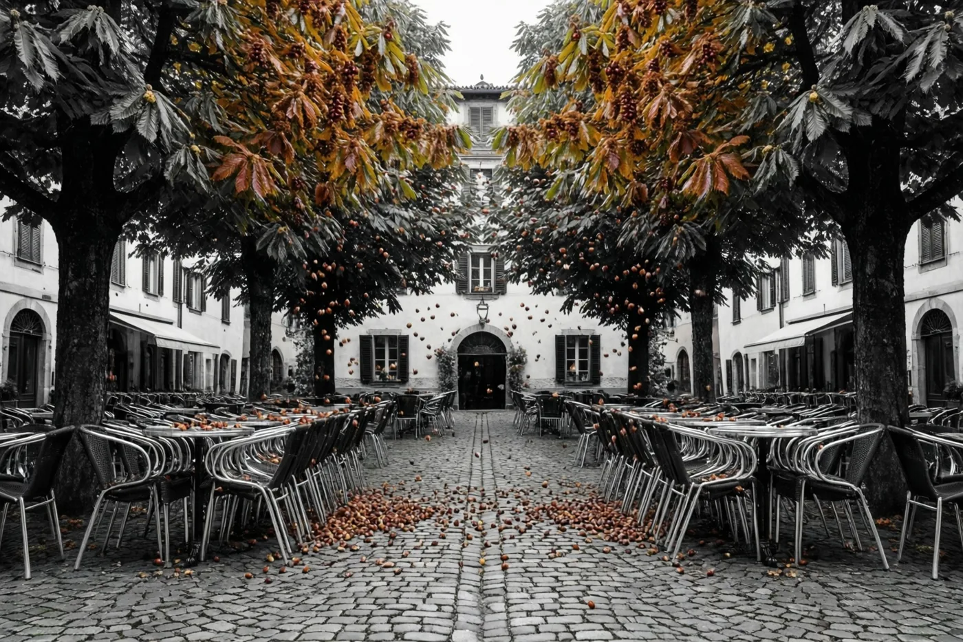 Kastanjebomen in herfstkleuren laten kastanjes vallen op een gekasseid dorpsplein en gestapelde caféstoelen, met warme kleuren tegen een monochrome achtergrond.