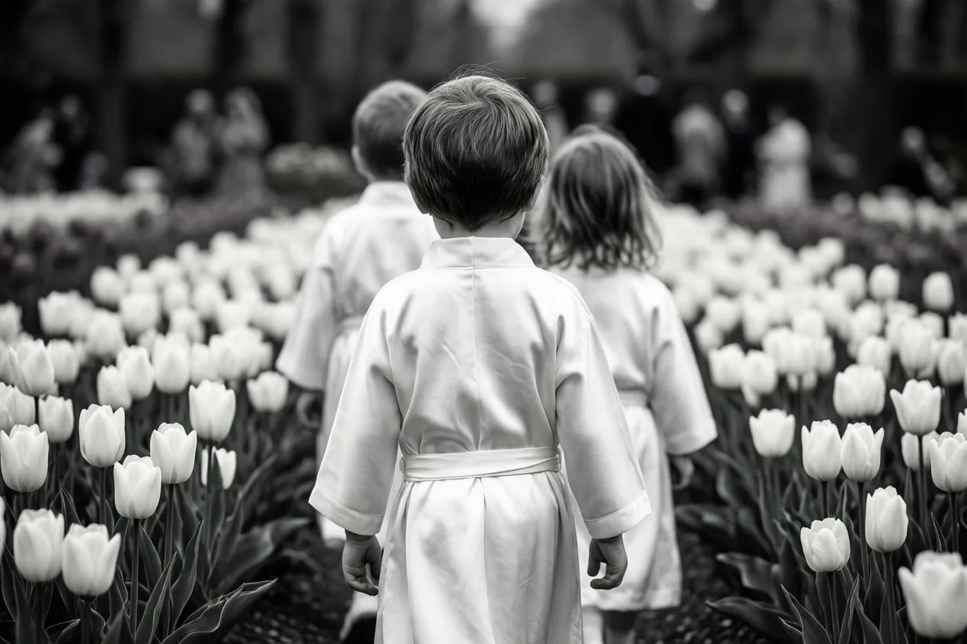 Op een zwart-witfoto lopen drie kinderen in witte gewaden van de camera weg door een veld met witte tulpen.