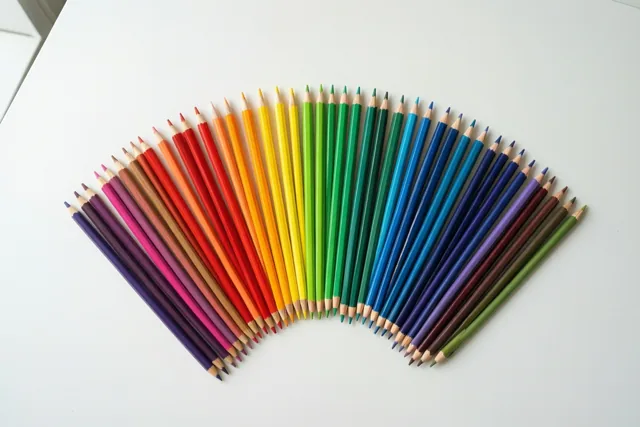 Kleurpotloden in de kleuren van de regenboog liggen in een waaier op een wit bureau.