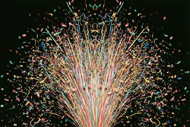 Rode, gele, blauwe en groene slingers en confetti waaieren vanuit het midden onderaan uit tegen een effen zwarte achtergrond.