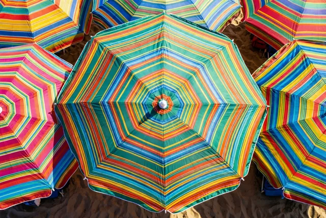 Van bovenaf zijn verschillende kleurrijk gestreepte strandparasols op het zand te zien.