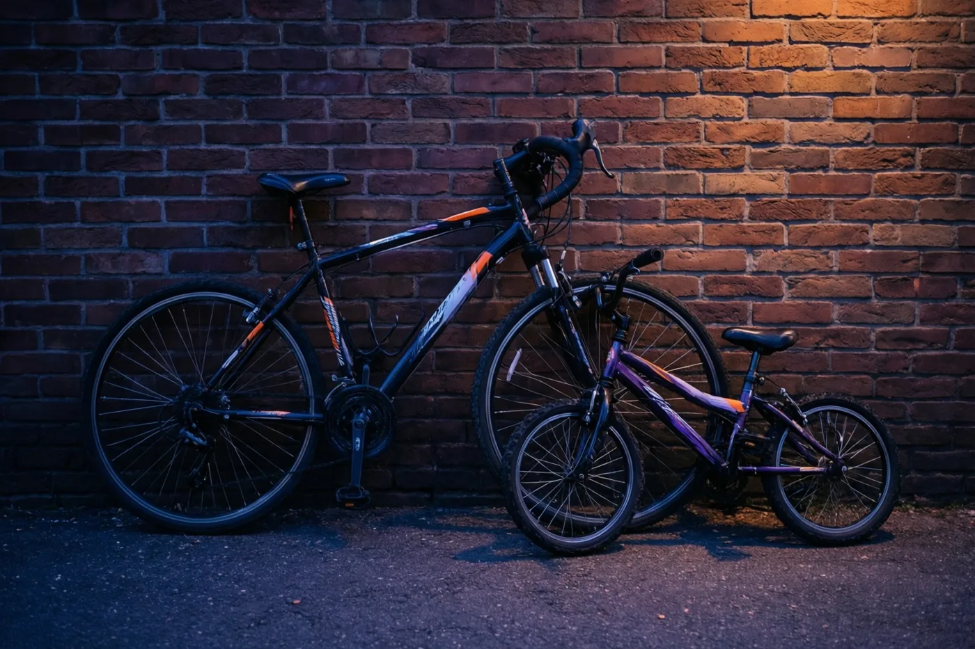 Een grote koersfiets en een kleine kinderfiets leunen naast elkaar tegen een bakstenen muur in warm oranje en koel blauw licht.