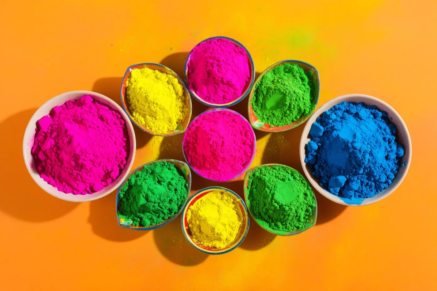 Kleine kommen met roze, geel, groen en blauw poeder staan op een feloranje ondergrond.
