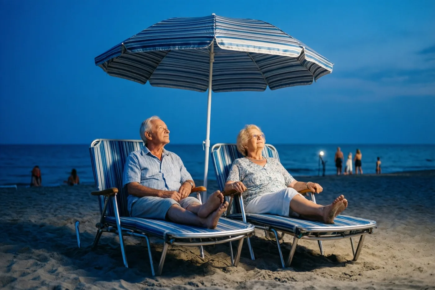 Een ouder koppel zit bij schemering op gestreepte strandligstoelen onder een bijpassende gestreepte parasol en kijkt naar zee, in blauwe en goudkleurige tinten.