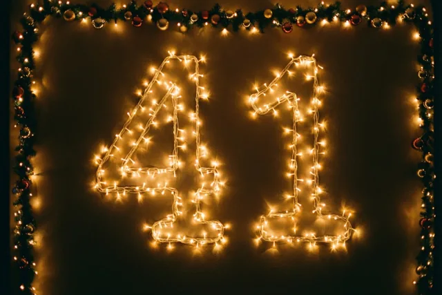 Warme lichtjes vormen 41 op een donkere muur, omlijst door een versierde slinger in gouden en rode tinten.