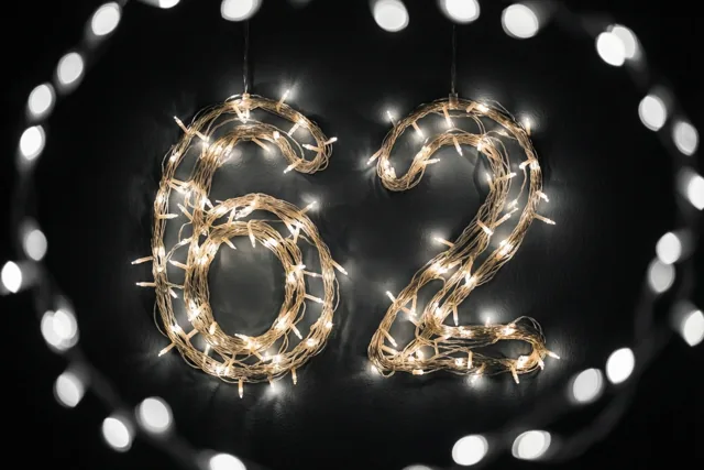Warme lichtslingers vormen 62 tegen een donkere muur, omringd door onscherpe lichtjes in witte en gouden tinten.
