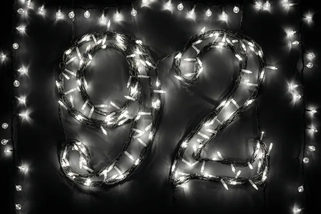 Lichtjes vormen 92 op een donkere muur, met warme onscherpe lichtvlekken rondom.