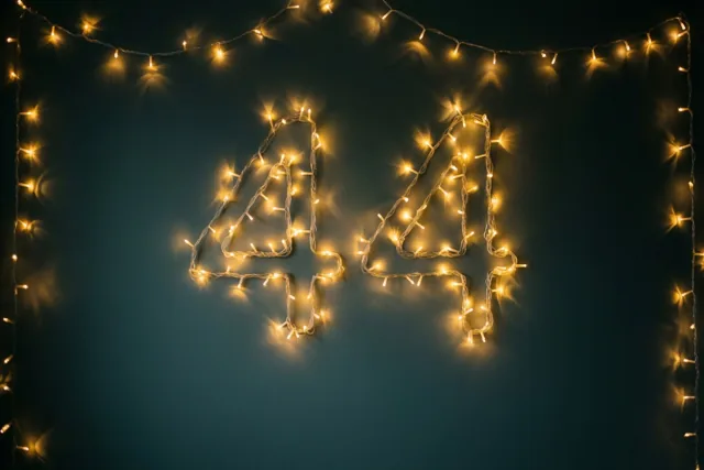 Warme lichtslingers vormen 44 tegen een donkere muur, omringd door extra lichtslingers en onscherpe lichtpuntjes.