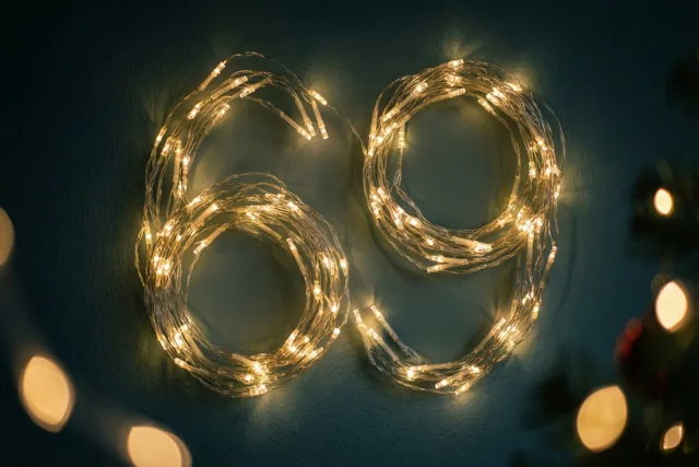 Warme lichtslingers vormen 69 tegen een donkere muur met onscherpe lichtjes op de achtergrond.