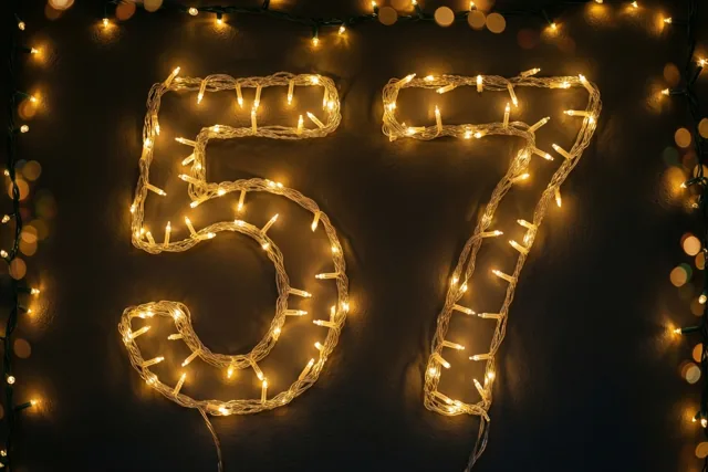Warm gloeiende lichtjes vormen 57 op een donkere muur met structuur, met onscherpe feestlichtjes op de achtergrond.