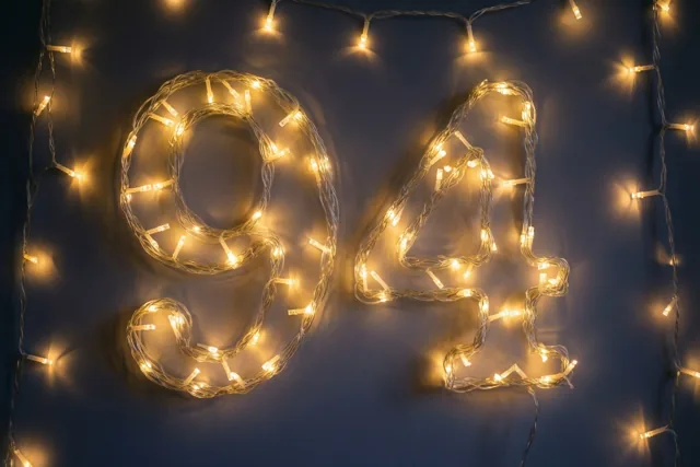 Warme lichtjes vormen 94 tegen een donkerblauwe muur, met zachte onscherpe lichteffecten.