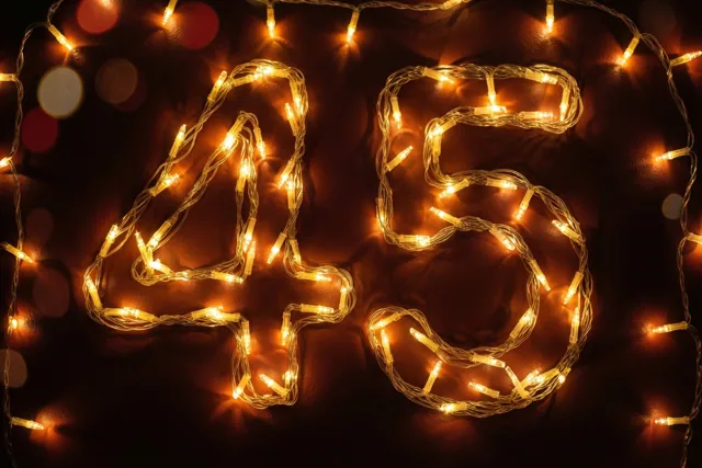 Het getal 45 is gevormd uit warm gloeiende lichtjes tegen een donkere muur, met onscherpe lichtvlekken erachter.