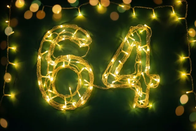 Warme lichtslingers vormen het getal 64 tegen een donkergroene muur, met onscherpe lichtjes op de achtergrond.