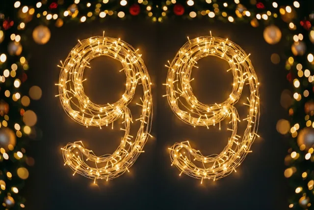 Warme lichtjes vormen het getal 99 tegen een donkere muur, omringd door onscherpe feestlichtjes in gouden en donkere tinten.