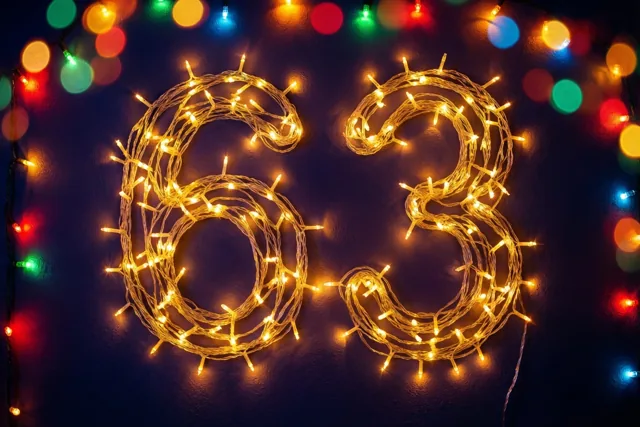 Warme lichtslingers vormen 63 tegen een donkere muur met kleurrijke onscherpe feestlichtjes op de achtergrond.