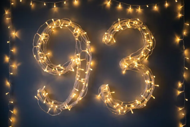 Het getal 93 is gemaakt van warme lichtjes tegen een donkere muur, met extra lichtslingers langs de randen.