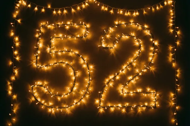 Lichtjes vormen het getal 52 op een donkere muur, omringd door extra lichtsnoeren en onscherpe lichtvlekken.