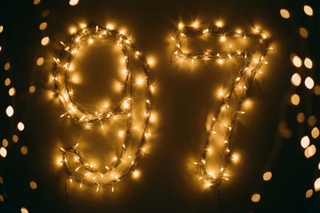 Het getal 97 is gevormd met warm gloeiende lichtslingers voor een donkere muur en een achtergrond met wazige lichtjes.