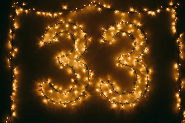 Het getal 33 is gevormd uit warme lichtslingers op een donkere muur en wordt omringd door een rand van lichtjes.