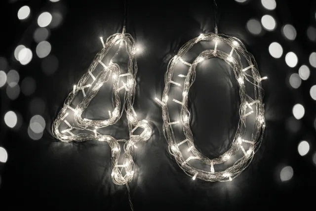 Lichtjes vormen 40 tegen een donkere muur, met wazige feestlichtjes op de achtergrond in een monochroom beeld.