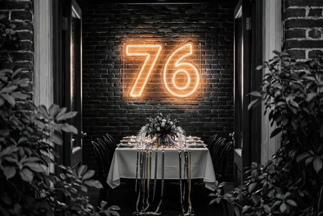 Een warm verlicht neongetal 76 hangt aan een donkere bakstenen muur boven een gedekte feesttafel, omkaderd door bladeren en deuropeningen.