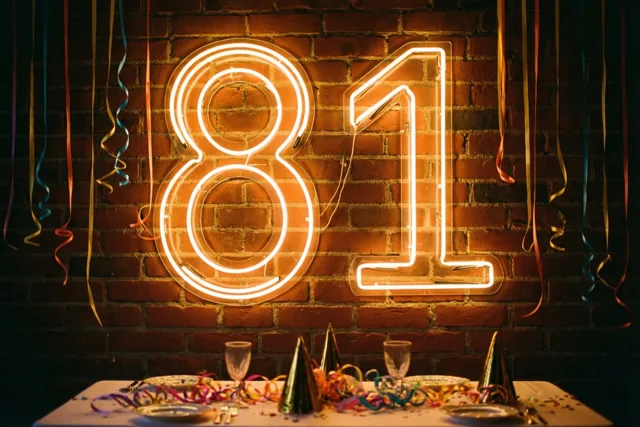 Een neonbord met het getal 81 licht warm op tegen een bakstenen muur boven een feesttafel met kleurrijke slingers en feestelijk servies.