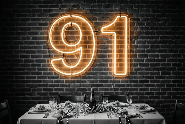 Een oranje neongetal 91 verlicht een donkere bakstenen muur boven een feestelijk gedekte tafel in zwart en wit.