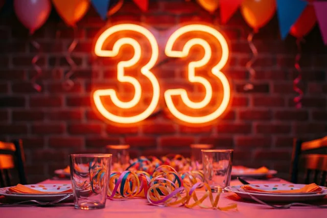 Een neoncijfer 33 hangt tegen een bakstenen muur boven een feesttafel met slingers, in warm rood en oranje licht.