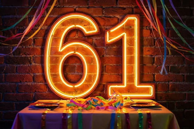 Een groot neongetal 61 gloeit boven een gedekte feesttafel met kleurrijke serpentines tegen een rode bakstenen muur.