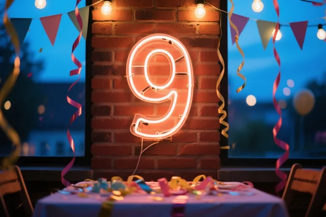 Een lichtgevende neonnegen hangt aan een rode bakstenen muur boven een feesttafel met kleurrijke slingers, met lichtslingers en vlaggetjes in de schemerige achtergrond.