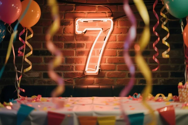 Een lichtgevend neoncijfer 7 hangt aan een rode bakstenen muur boven een feesttafel met confetti en slingers, met ballonnen en kleurrijke slingers op de voorgrond.