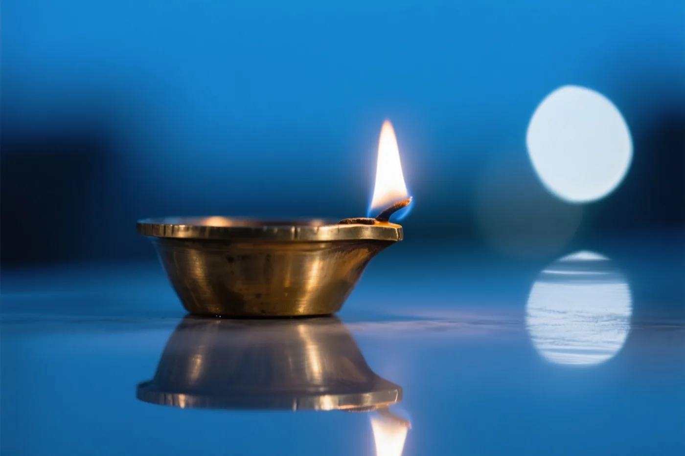 Een brandend olielampje weerspiegelt in een gepolijst oppervlak tegen een blauwe achtergrond met wazige lichtpuntjes.