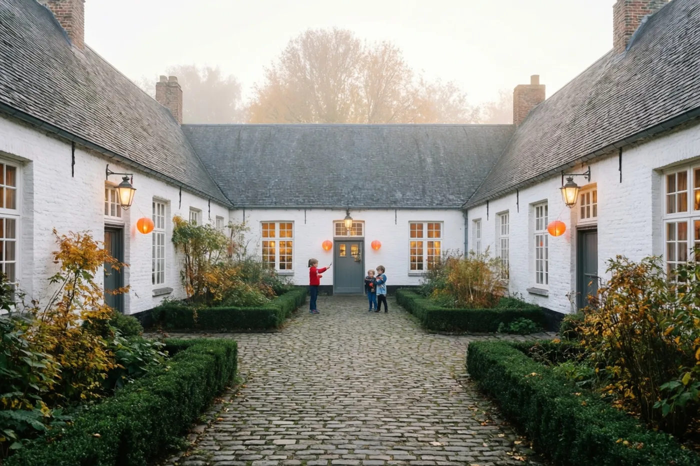 Kinderen met oranje papieren lampionnen verlichten een binnenplein met witgekalkte gebouwen en een kasseienpad op een mistige avond, omgeven door herfstbladeren en verlichte ramen.
