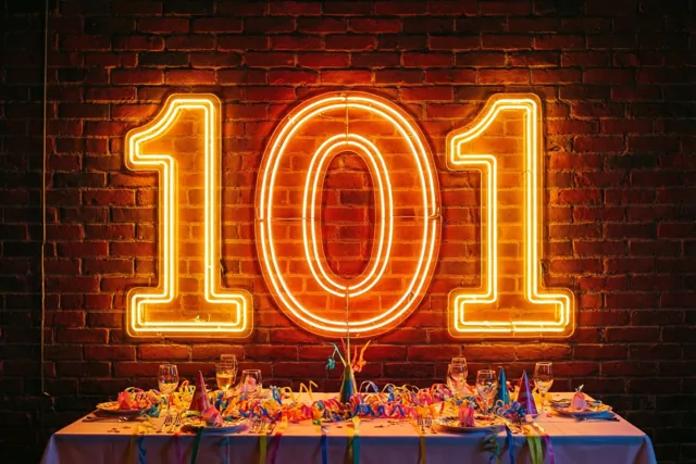 Een neonbord met 101 in warm oranje licht hangt aan een rode bakstenen muur boven een feestelijk versierde tafel.